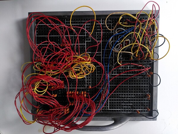 A kind of old and metal black motherboard, full of yellow, red and blue cables over a white background